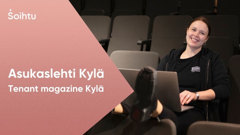 Nainen istuu tietokoneen kanssa ja hymyilee kameralle.